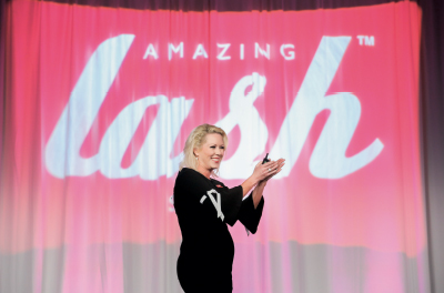 CEO Heather Elrod clapping in front of logo on stage at conference