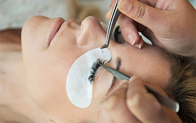 Guest relaxes with eyes closed while stylist applies eyelash extensions